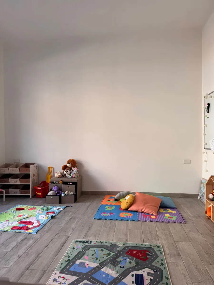La sala giochi di Little Steps, con tappeti puzzle, cesti di peluche e lavagna